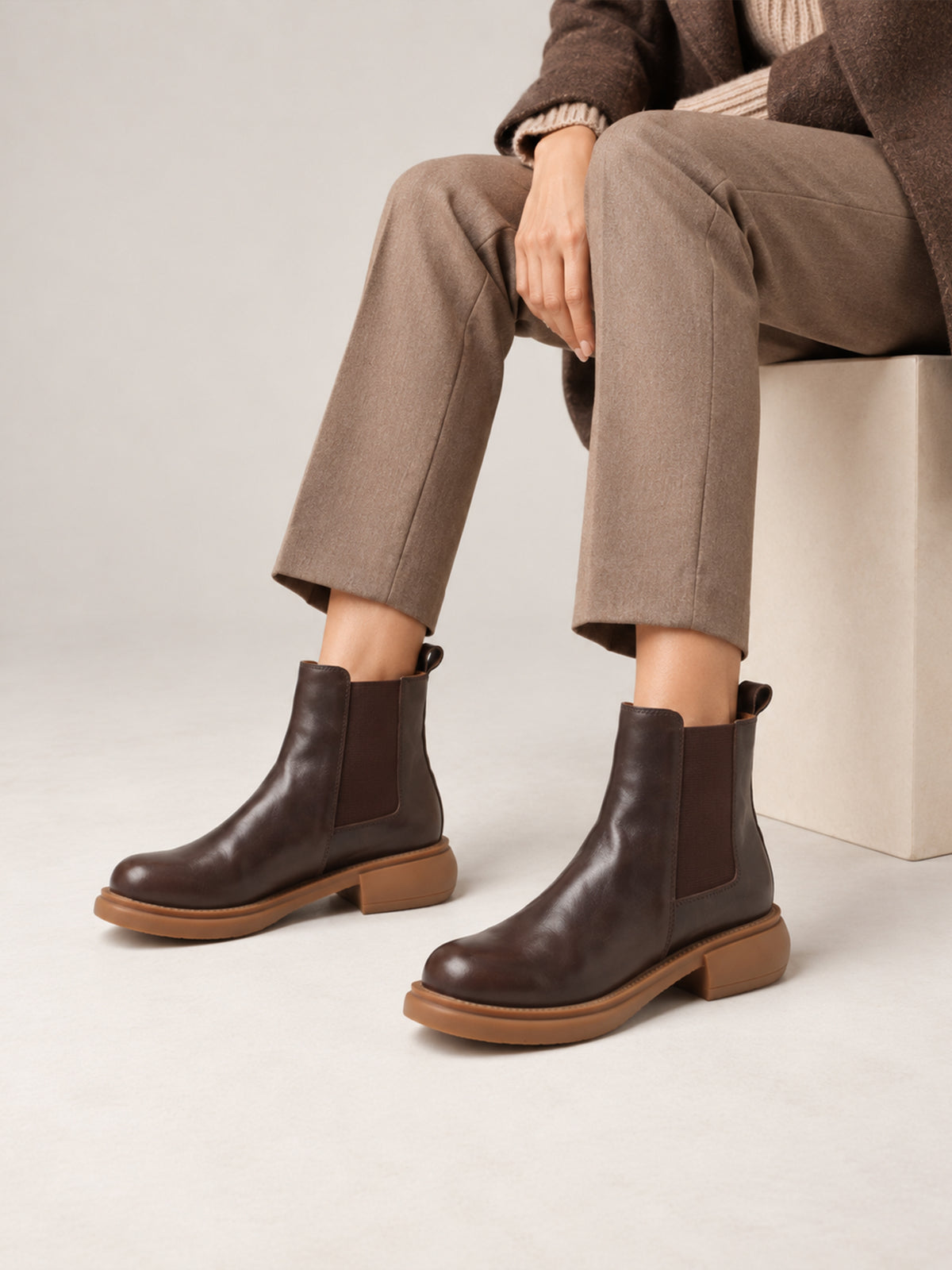 Dark brown washed-leather Chelsea boots, close-up of the boots worn with taupe trousers.
