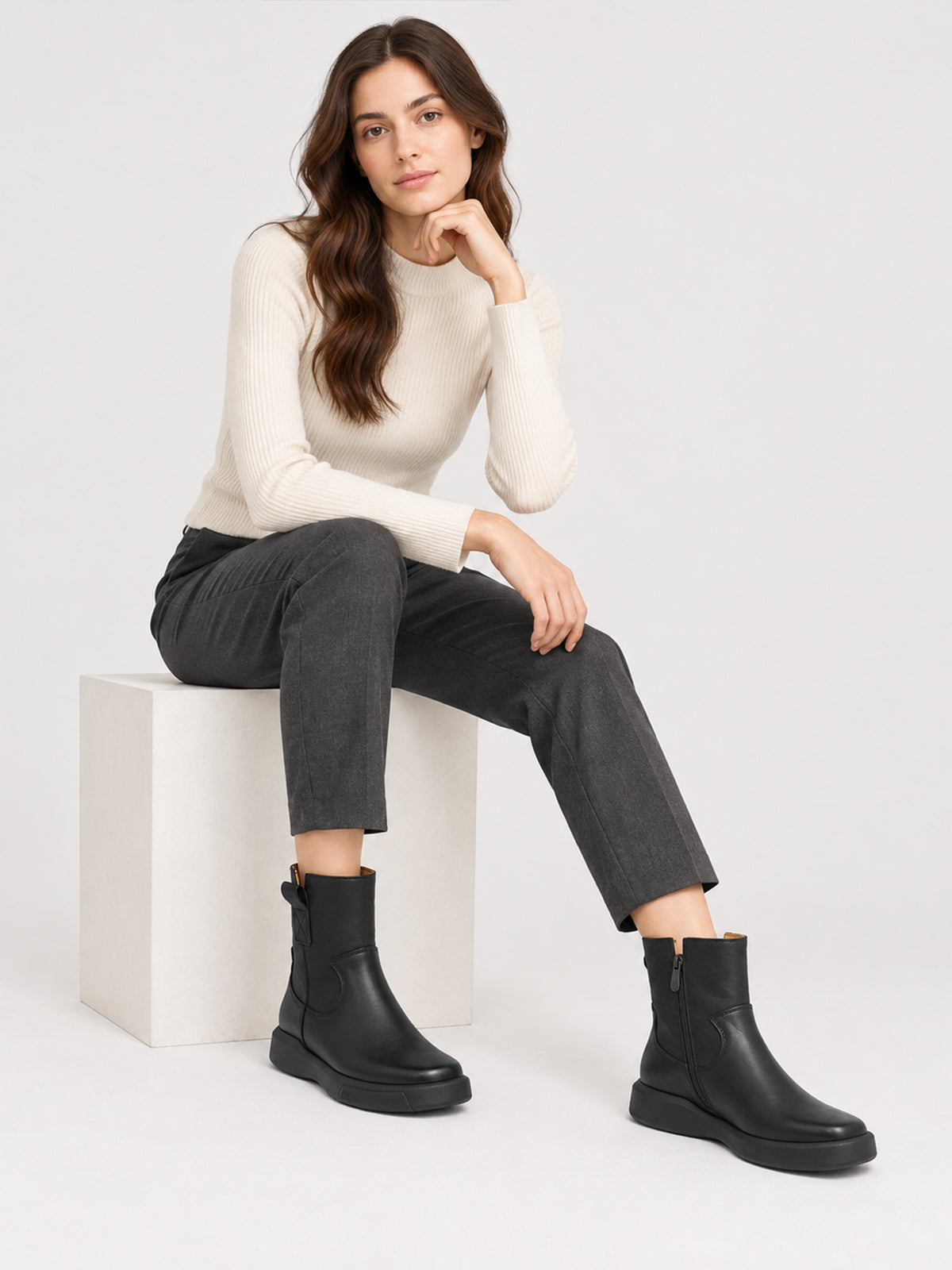 Black zip ankle boots, worn in a seated outfit.