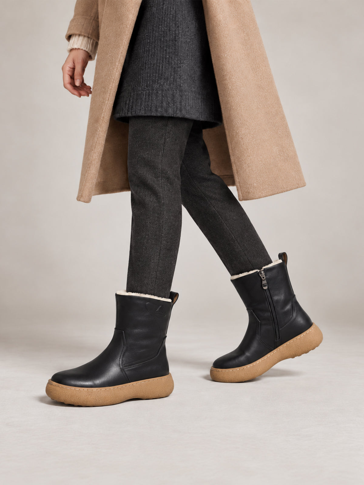 Black polished winter boots with tan soles, close-up of the shoes being worn.
