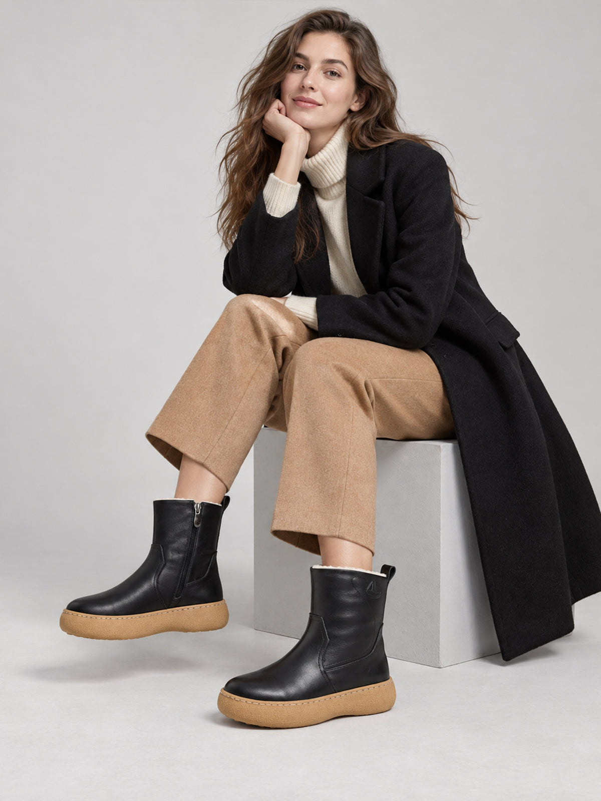 Black polished winter boots with tan soles, worn in a seated outfit.