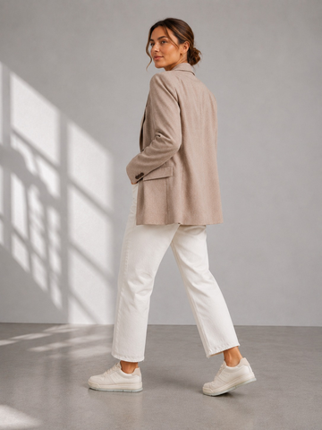 Rear angled view of cream sneakers worn with white trousers and a beige blazer.