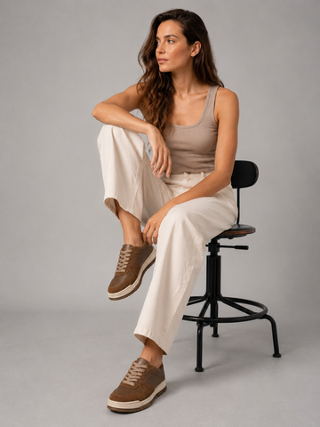Woman adjusting a brown sneaker while seated on a studio stool.