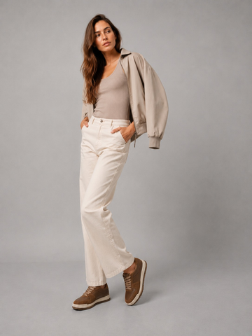 Woman wearing brown sneakers with cream trousers and a light jacket against a studio background.
