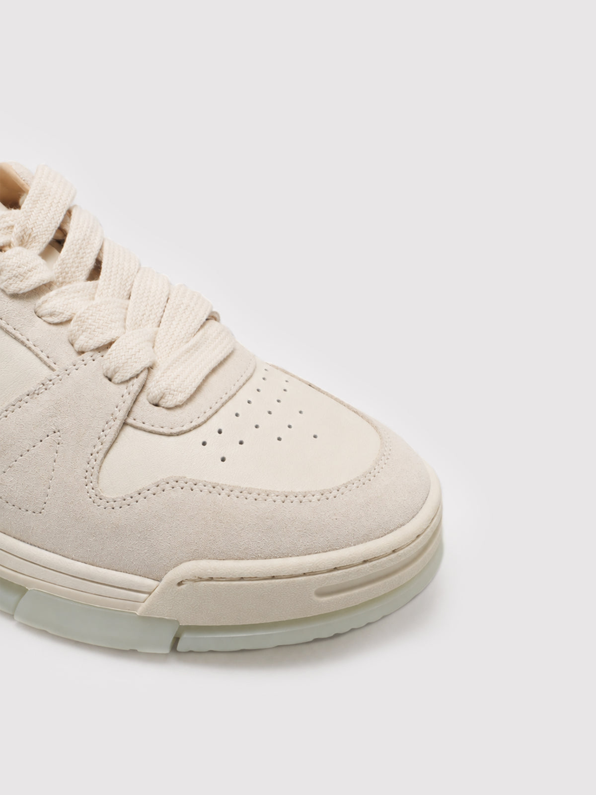 Close-up of the perforated toe and laces of a cream sneaker.