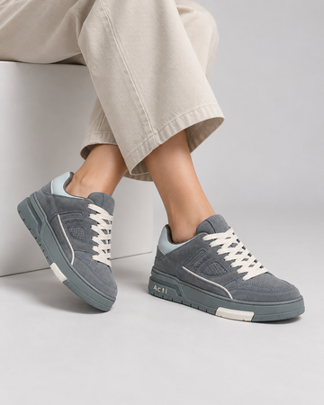 Gray lace-up sneakers, worn with cream trousers while seated.
