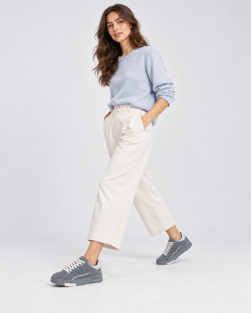 Gray lace-up sneakers, walking view with light trousers and a blue shirt.