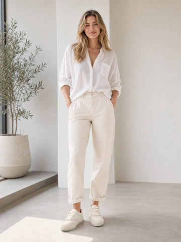 Woman wearing cream sneakers with a white shirt and cropped cream trousers.