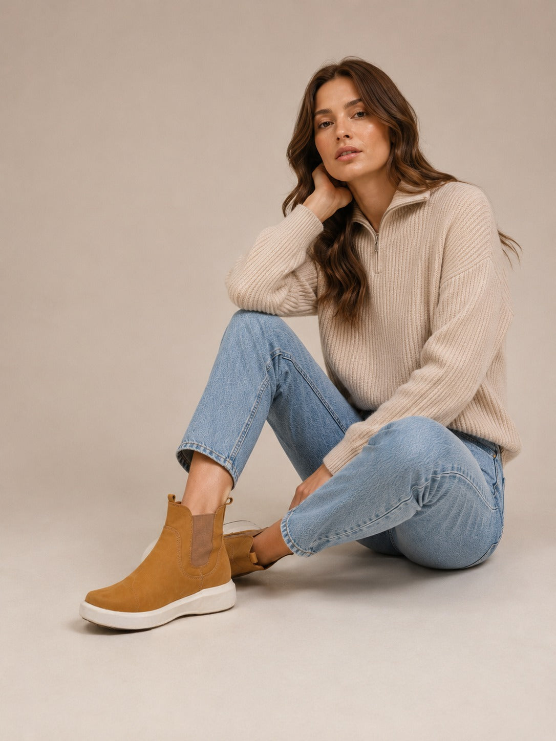 Golden tan nubuck Chelsea boots from the Block Series, worn with jeans and a cream sweater while seated.